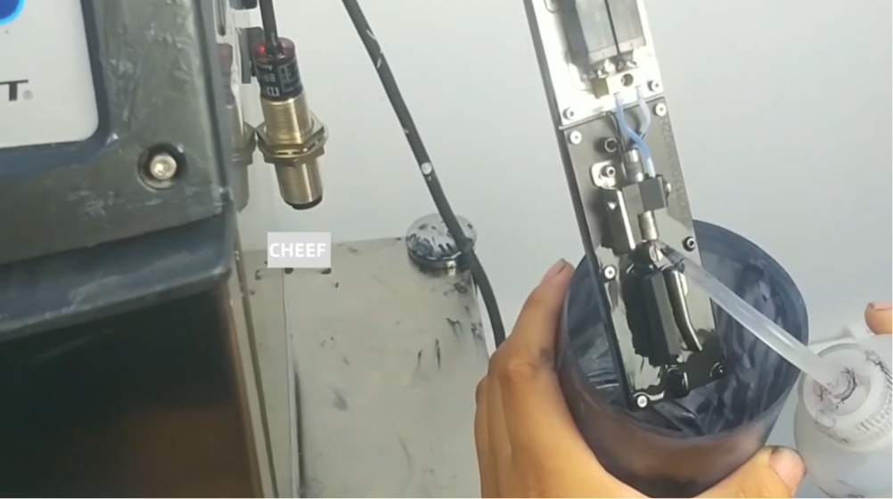 Technician performing maintenance on a Videojet 1000 Series continuous inkjet (CIJ) printer, carefully cleaning printer components to troubleshoot recovery failure and restore proper operation.